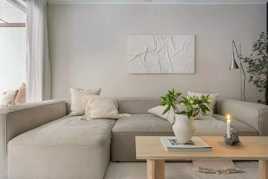 White wall relief with irregular folded shapes above a cream sectional sofa