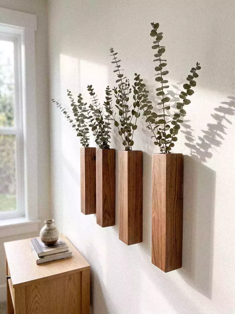 Wooden wall-mounted vases with eucalyptus stems beside a sunlit window