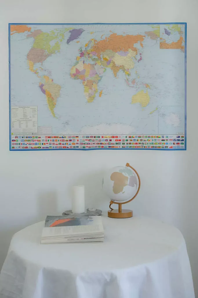 World Map Wall Decor Above A White Covered Round Table With A Small Globe And Stacked Books